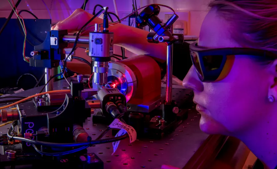 Female photonics degree student wearing glasses and staring into machine