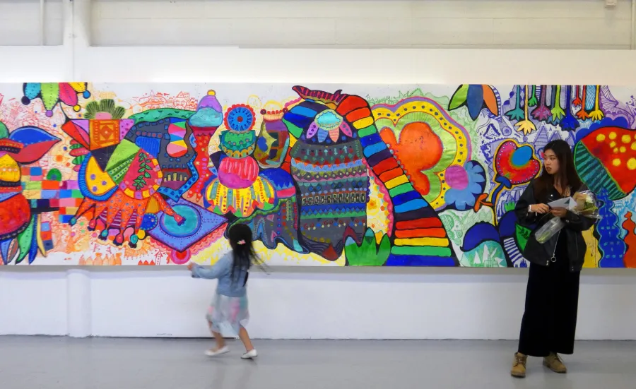 A student standing in front of a colourful mural which covers an entire wall at Winchester School of Art
