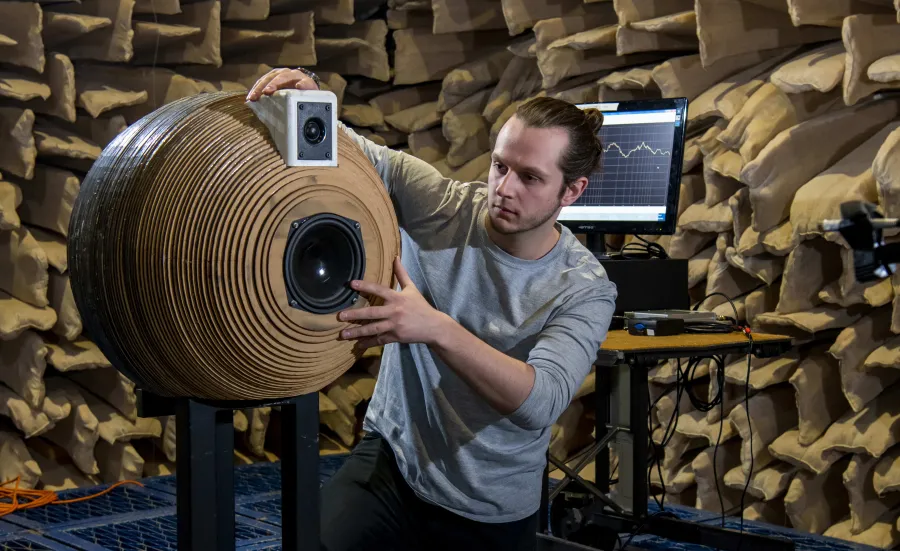 A student positioning a novel, spherically-designed speaker system inside the large anechoic chamber for testing.