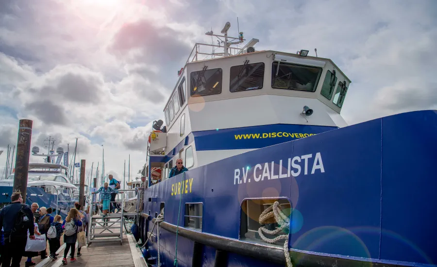 An industrial looking boat emblazoned with the name RV Callista, moored beside a wooden dock, beneath a sunny sky.