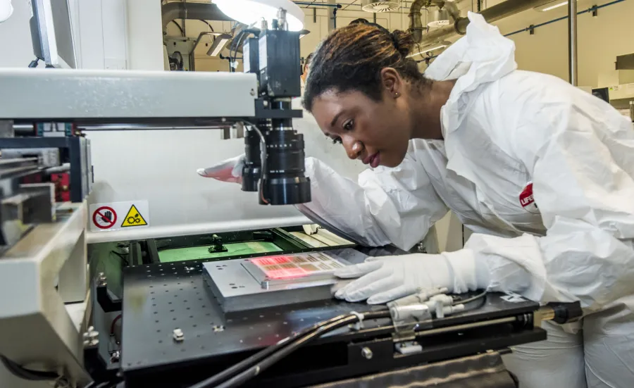 A student wearing protective clothing uses printed electronics and materials equipment