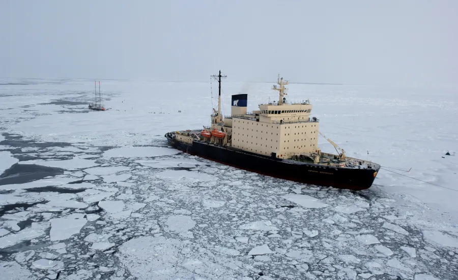 A ship surrouded by ice next to a small vassel.