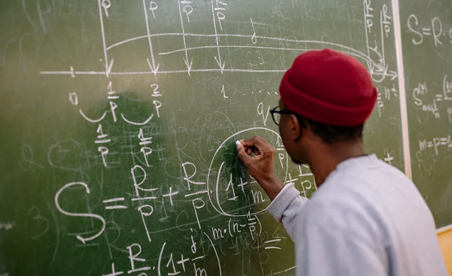 A person with their back to us works out a maths equation on a chalkboard