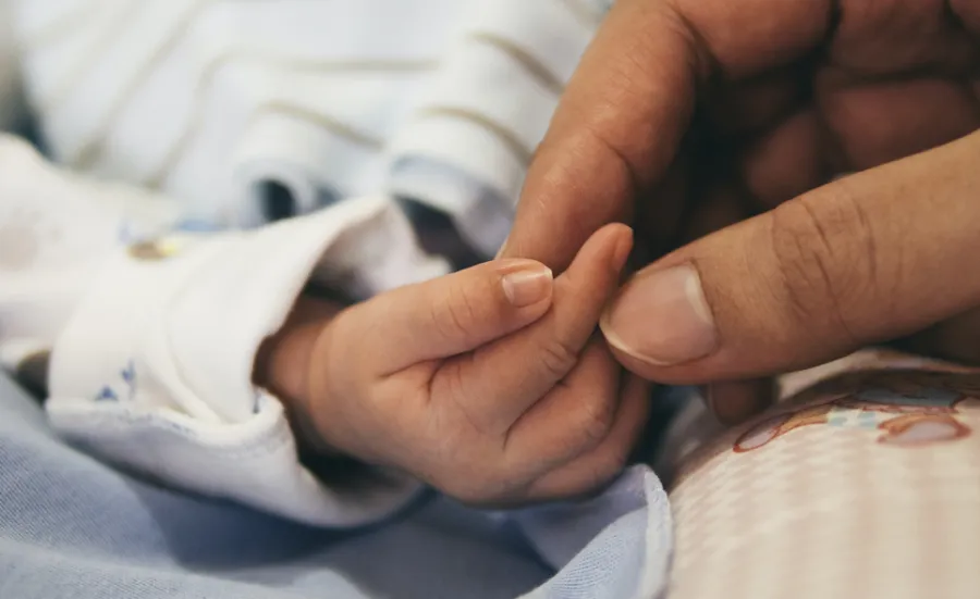 An adult hand gently clasps the hand of a small child