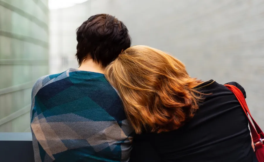 Two people sitting down, facing away from us. One is leaning into the other.