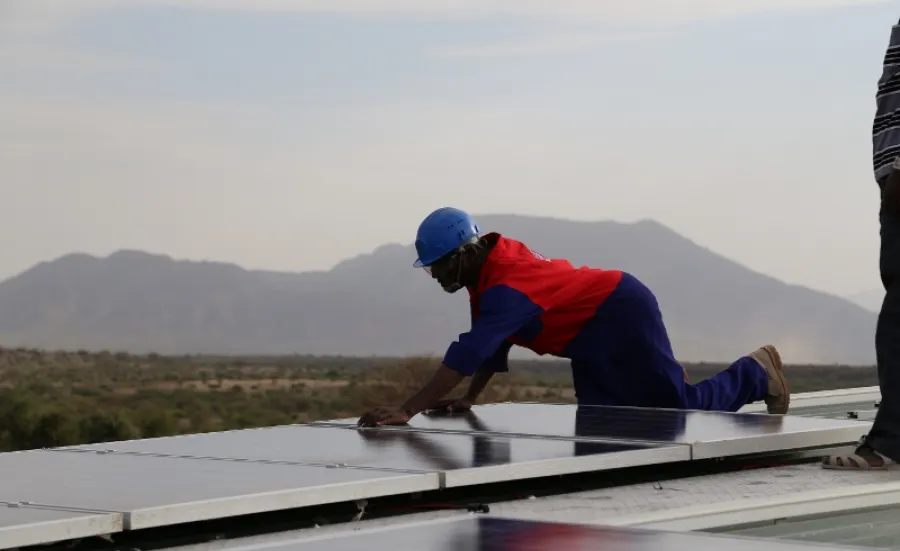 person wearing construction clothing fitting solar panels for renewable energy on roof in kenya