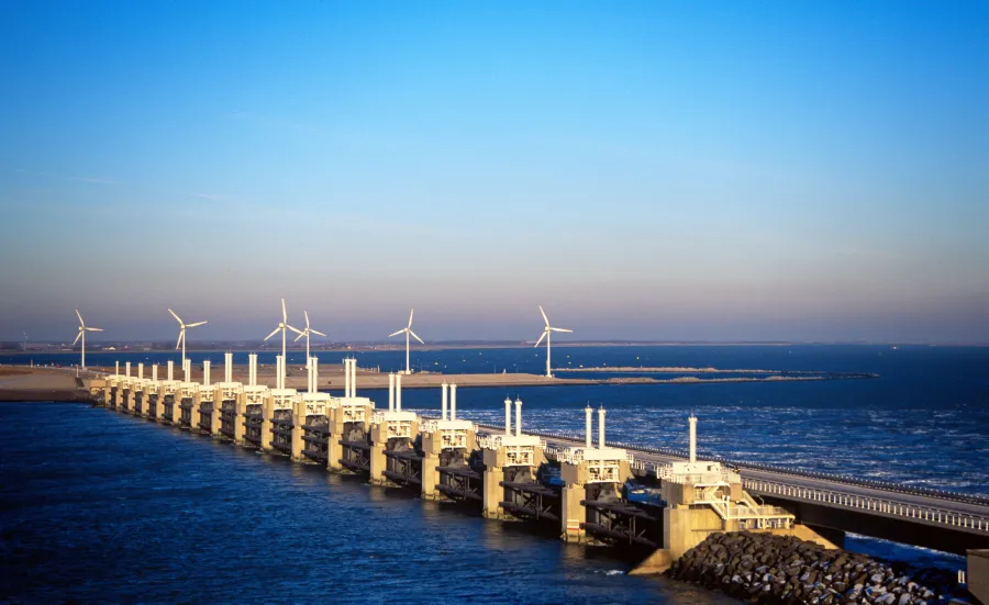 A wide shot of a storm surge barrier, with several wind turbines spinning in the background.
