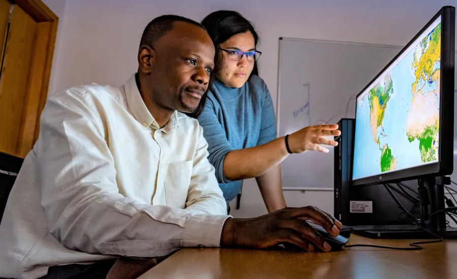 Two researchers stare intently at a screen with geographic information, one pointing to a specific area