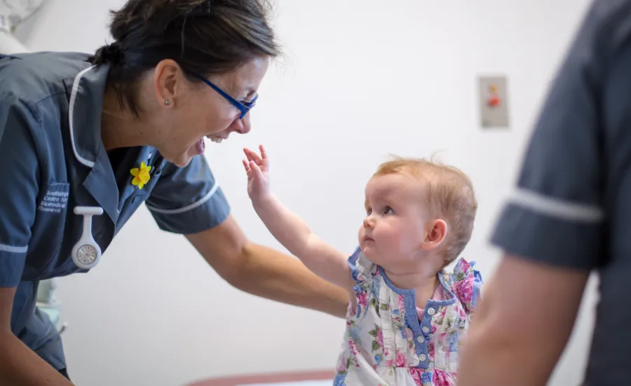 Baby reaches up towards smiling research nurse 