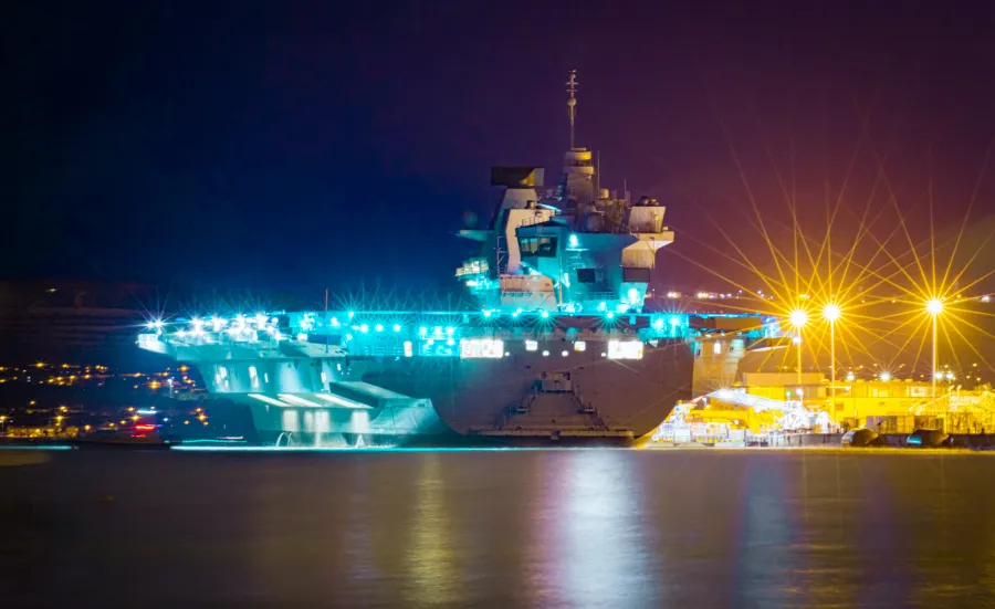 Aircraft carrier lit up at night in dock