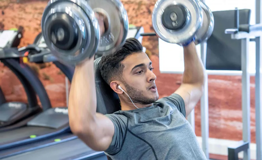 A student lifts weights above his head, he looks determined