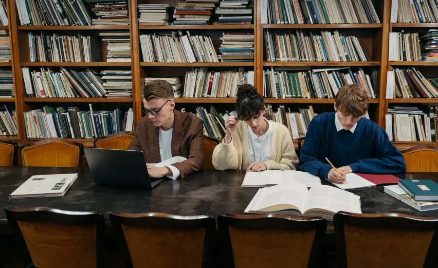 Three young researchers in an old library taking notes