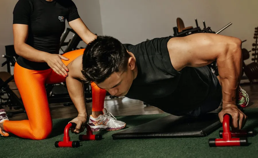 A personal trainer gives advice to a gym user doing press ups