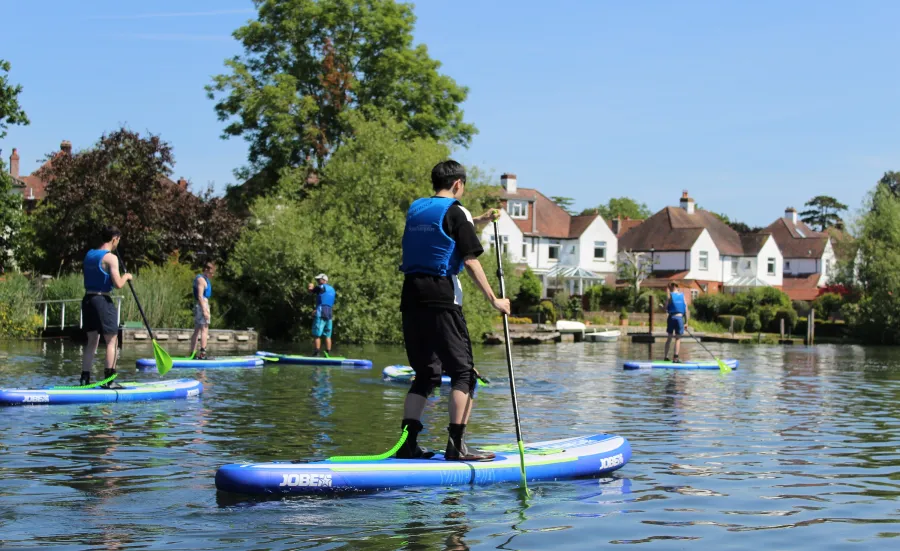 A group of young people paddleboarding on a river on a sunny day