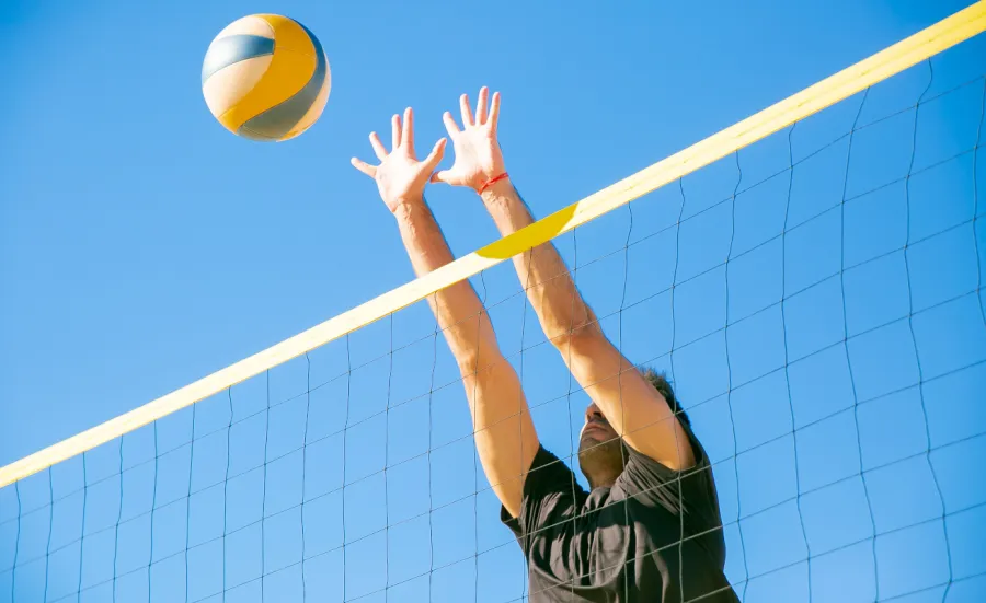 Man hitting volleyball over a net outside