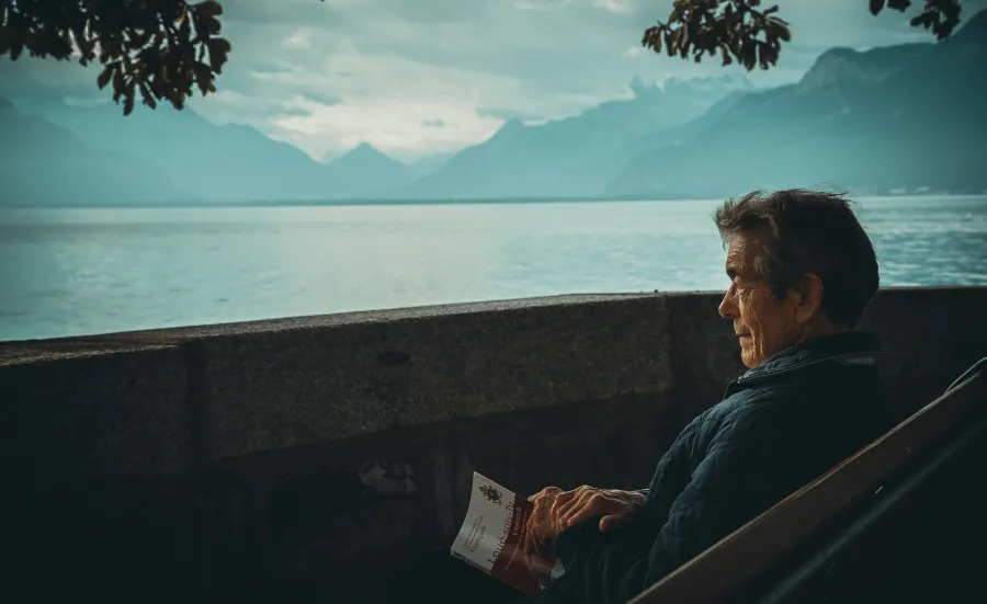 Elderly man sat on a bench next to an alpine lake