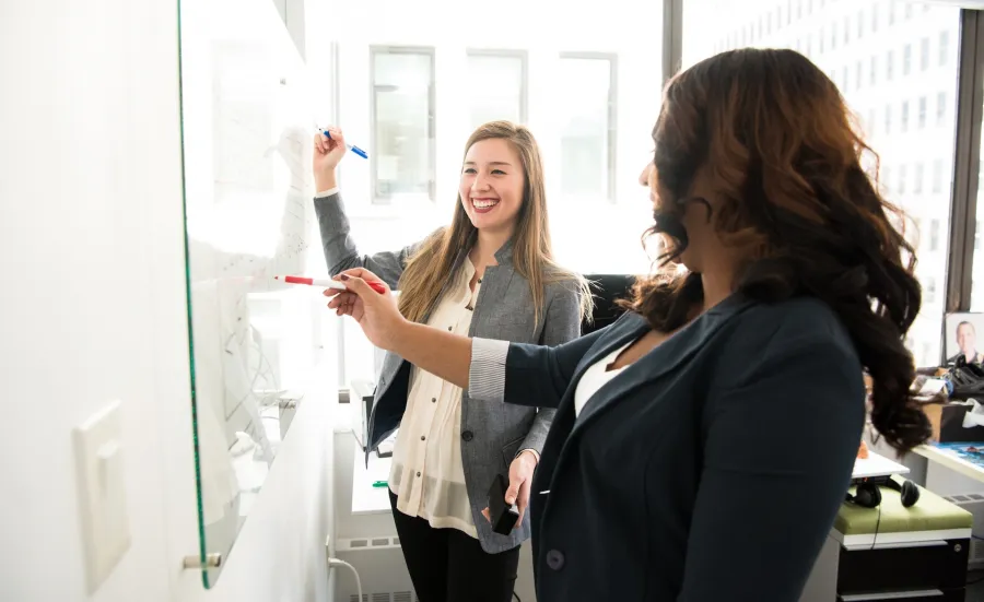 Two women in an office writing on a whiteboard