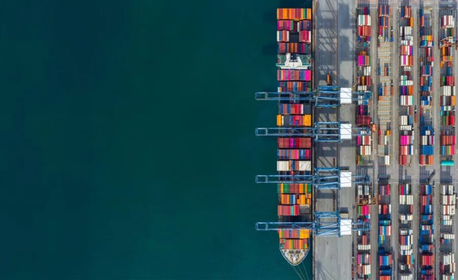 Top-down view of colourful shipping containers at a seaport with clear water