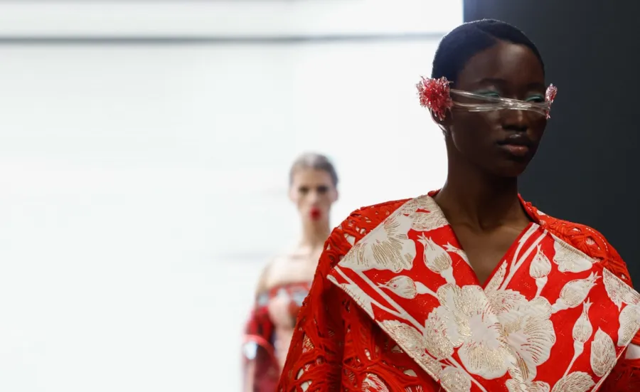 A catwalk model sports a dramatic red and white creation featuring a floral motif and outsized lapels