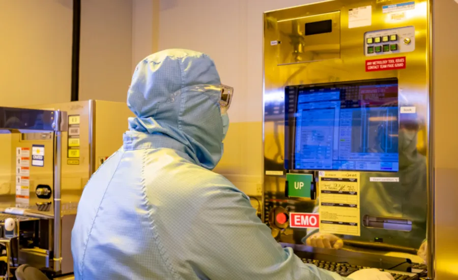 A researcher in a cleanroom suit sits with their back to the camera, using the Critical Dimension Scanning Electron Microscope (CD-SEM) 