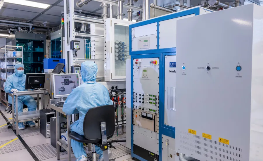 Two researchers in cleanroom suits sit at computers in the nanofabrication ballroom cleanroom