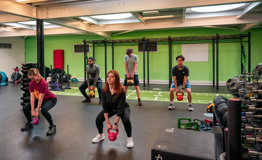 People in a gym lifting a kettlebell from a squatting position