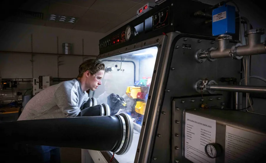 A researcher wearing safety goggles works with chemicals in a glovebox