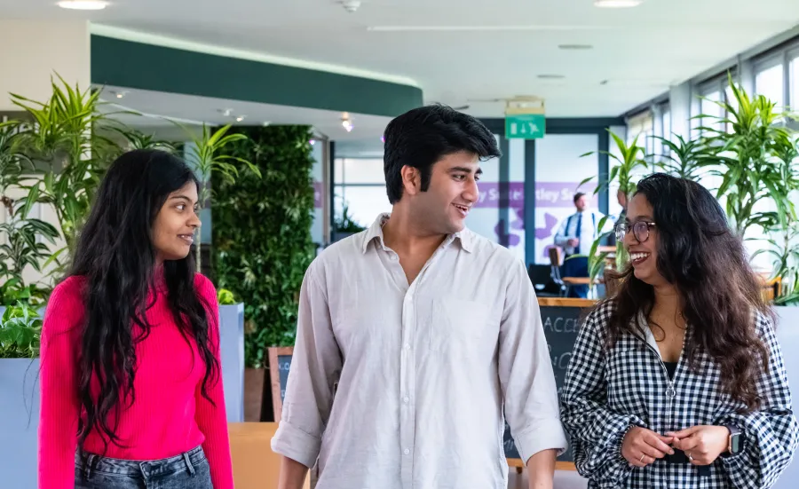 Three Indian students walking and talking in a green, plant-filled indoor space