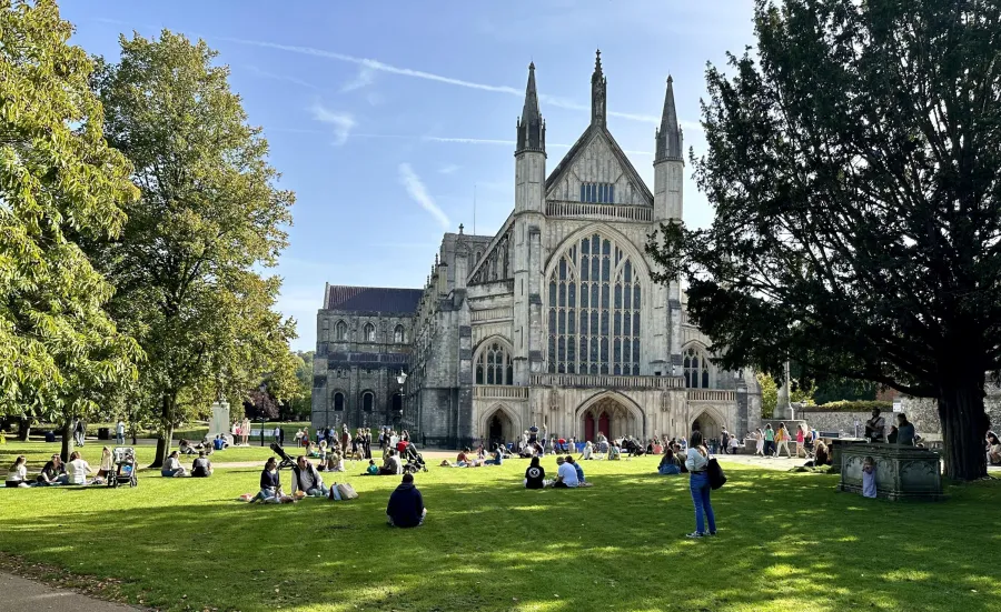 Exterior of Winchester cathedral with several people sat in the surrounding grounds.