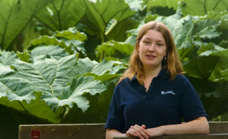 Student Adele, presents to camera from Valley Gardens on Highfield Campus. In the background large, green leaves are visible.