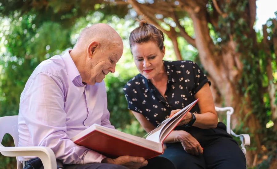 A woman and an elderly man sat in a park looking at a book together