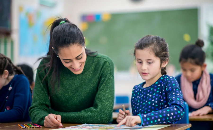 Adult sat with a child at a school desk with a drawing