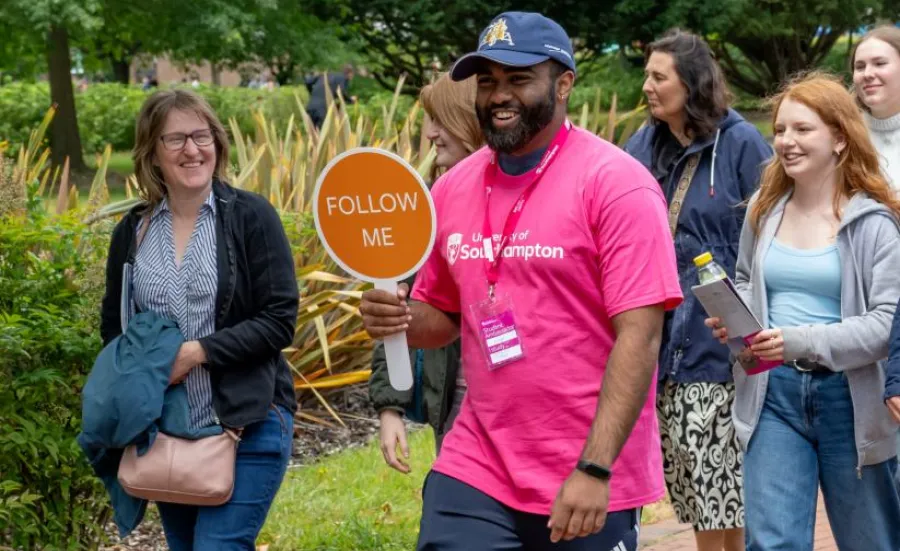 A student ambassador with a "Follow me" sign guides a visitor group on a tour of campus