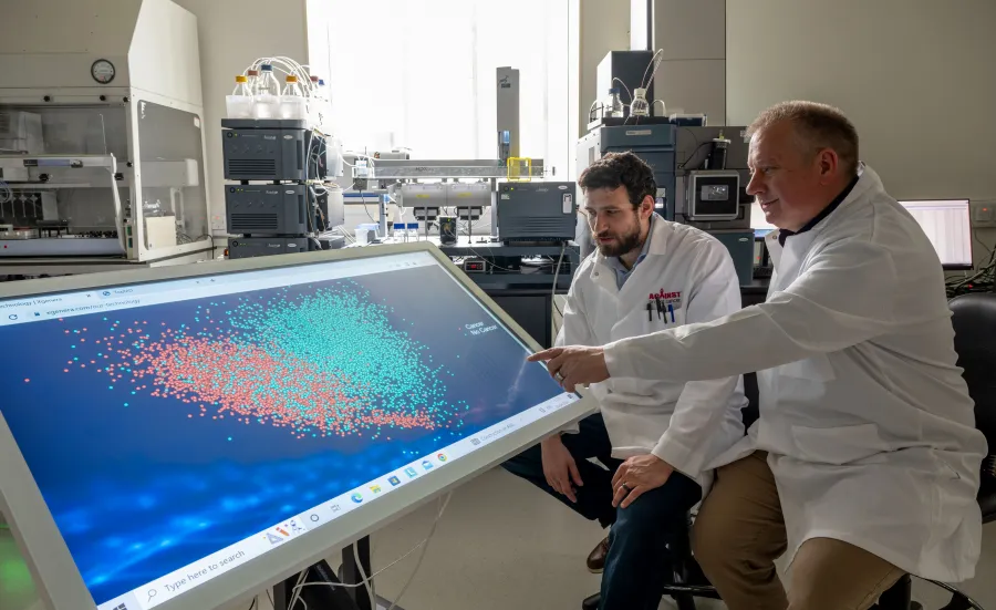 Two scientists observing blood test results on a screen. The results are colour coded in red and blue to show whether cancer is present or not.