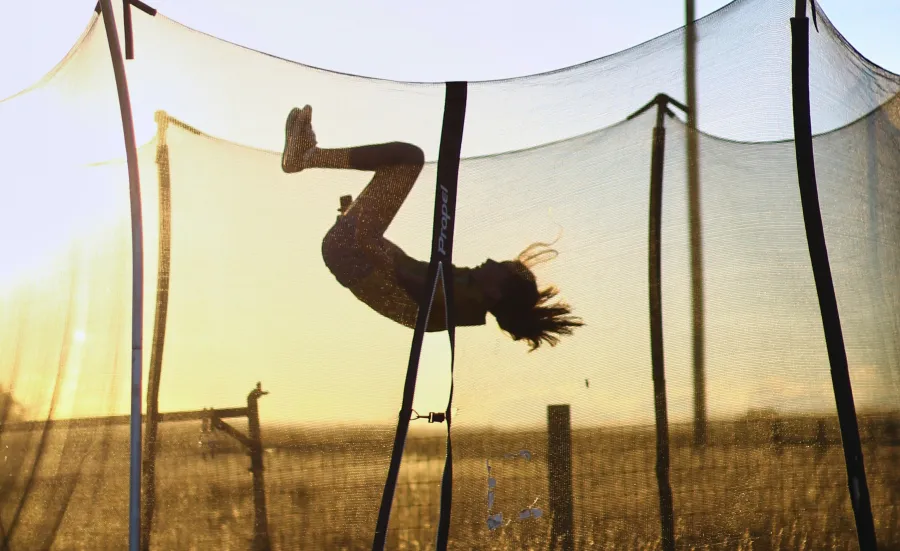 Child performing a flip on a trampoline during sunset in a field.