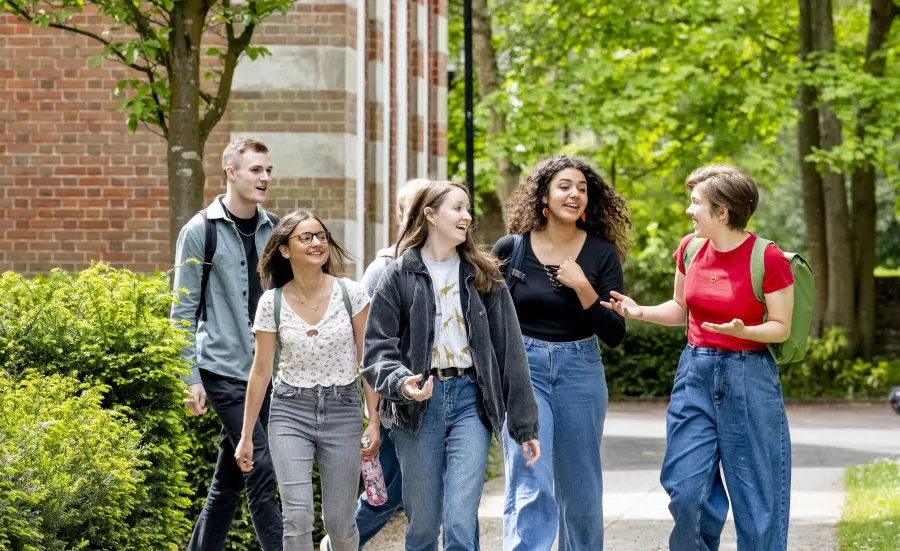 A group of students talking and walking along a path at Avenue campus. The trees are in full leaf and the sun is shining. 