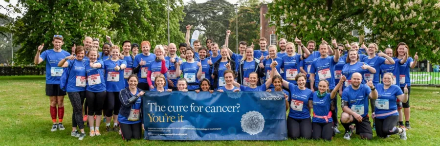 Around 50 participants in the 2017 ABP Southampton marathon cheering for the camera. Their banner reads: "The cure for cancer? You're it."