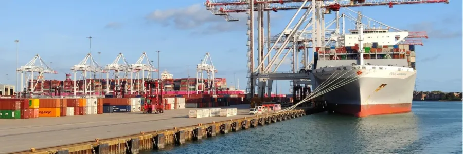 Cargo ship docked at a port with stacked containers and cranes against a clear sky