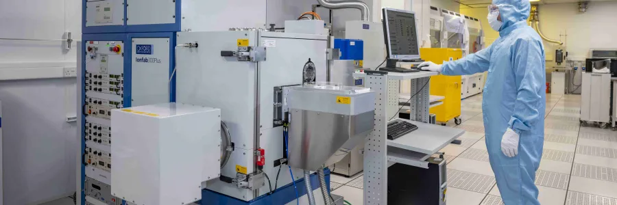 A researcher in a cleanroom suit in the integrated photonics cleanroom using the ion beam etch and deposition tool