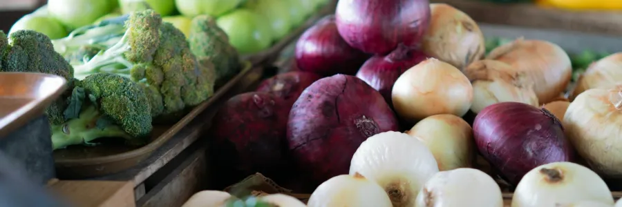 Assorted vegetables including onions, bell peppers, broccoli, and beetroot on a market stand.