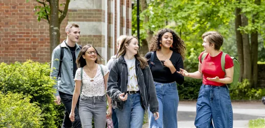 A group of students talking and walking along a path at Avenue campus. The trees are in full leaf and the sun is shining. 