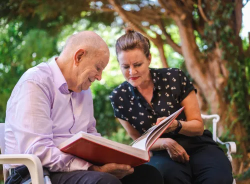 A woman and an elderly man sat in a park looking at a book together