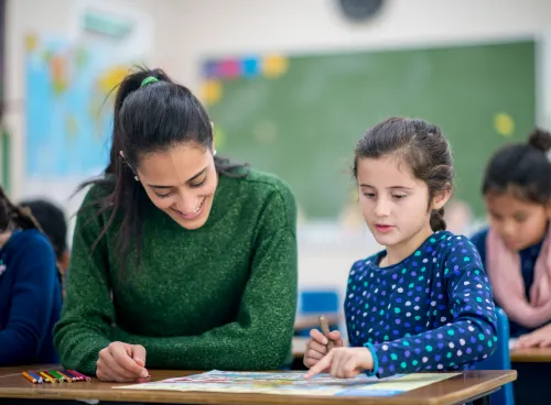 Adult sat with a child at a school desk with a drawing