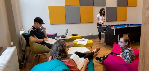 Group of students in common room, sat talking and playing pool.