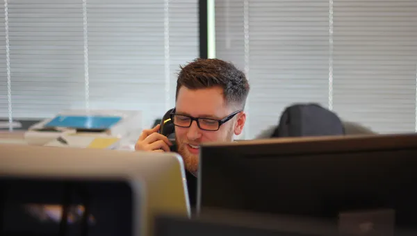 Man on phone in student support, looking over the top of a computer.