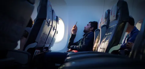 A man looks at his mobile phone while seated on a plane flight