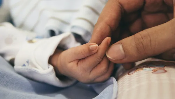 An adult hand gently clasps the hand of a small child