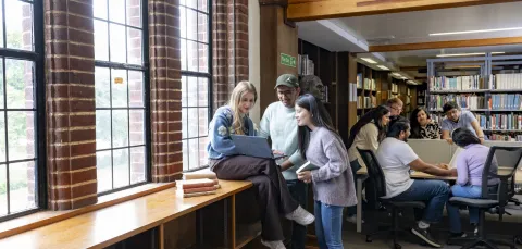 Two groups of students in the Hartley library. I group looking at a laptop and the other talking around a table.