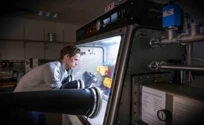 A researcher wearing safety goggles works with chemicals in a glovebox