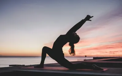 Silhouette of a person doing yoga by the water at sunset.